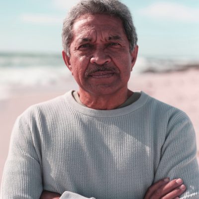 Portrait of retired biracial senior man with arms crossed at beach against sky during sunny day. active lifestyle and weekend. Portrait of retired biracial senior man with arms crossed at beach against sky during sunny day. active lifestyle and weekend.